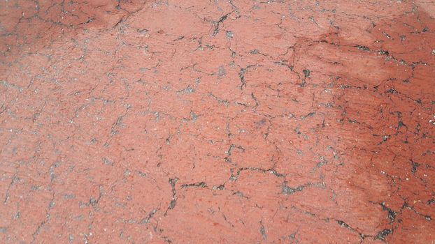 Red colored damaged road or paved pathway with crackes of different shpaes. Cracked texture with copy space for text and messages