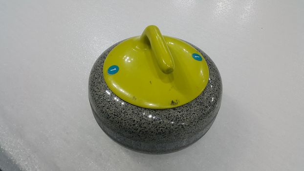 Top angular view of a curling stone on white slippery ice pitch in an arena for ice gmaes