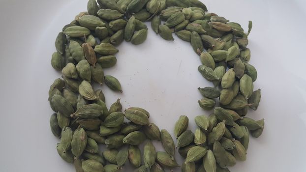 Closeup top view of dried green Elettaria cardamomum fruits with seeds, cardamom spice arranged in ring on a white background