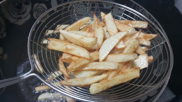 Closeup view of potato french fries or roasted potato sticks in metal gaze with copy space for text