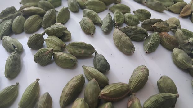 Closeup top view of dried green Elettaria cardamomum fruits with seeds, cardamom spice scattered on white background