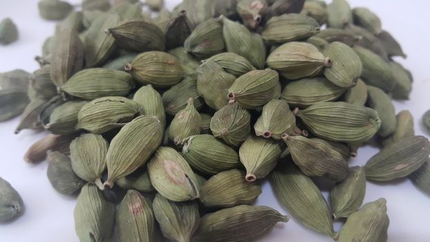Closeup top view of dried green Elettaria cardamomum fruits with seeds, cardamom spice scattered on white background