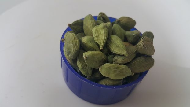 Closeup top view of dried green Elettaria cardamomum fruits with seeds, cardamom spice in small bowl on white background