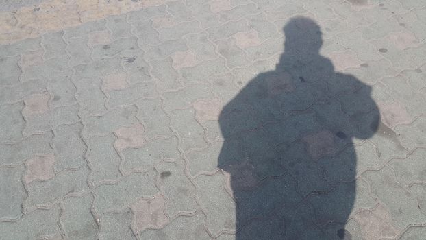 Silhouette: A Man's shadow on the red colored concrete ground under sunlight