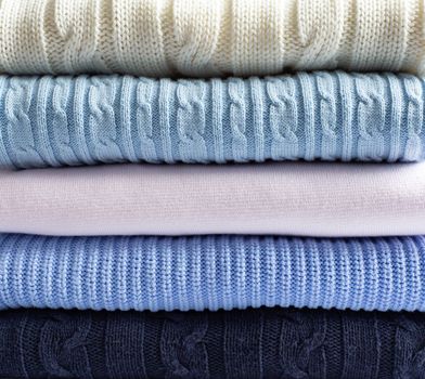 Pile of knitted winter woollen clothes sweaters of pastel colour. Cosy clothes