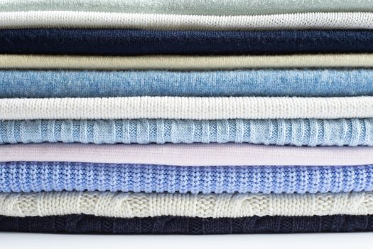 Pile of knitted winter woollen clothes sweaters of pastel colour. Cosy clothes made of wool silk cashmere, Close up