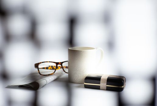 Cup of morning coffee, eyeglasses, wrapped gift box, newspaper with crossword on light background, soft focus. Happy Fathers Day concept