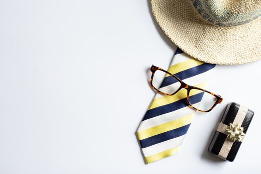 Mens yellow stripy tie, wrapped gift box, eyeglasses, straywsummer hat on white background. Flat lay, above view. Happy father's day concept