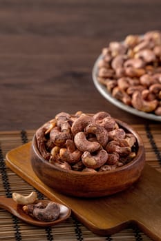 Cashew nuts with peel in a wooden bowl on wooden tray and table background, healthy raw food plate.