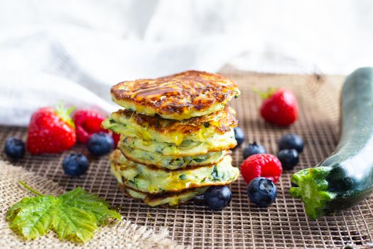 Fresh pile of delicious homemade courgette pancakes topped with honey maple syrup, summer fruits, zucchini and maple leaf on kitchen grill. Close up. Recipe, cooking, season, menu concept