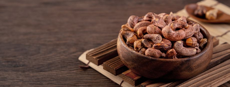 Cashew nuts with peel in a wooden bowl on wooden tray and table background, healthy raw food plate.