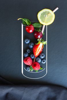 Summer fruits, berries, lemon, mint and straw in the cute chalk painted glass on black background with canvas. Healthy, vitamin, diettary food concept. Vegan, vegetarian and detox food and drinks. Menu mock up, poster concept