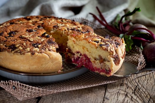 Homemade delicious beetroot pastry tart on kitchen grill with slice of cake and fresh beetroots on rustic wooden bakground. Menu, board, banner. Vintage traditional rustic kitchen. British meal