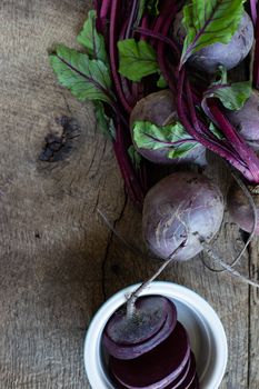 Bunch of fresh, spring, organic beetroot with slices of beetroot in ceramic plate on old wooden background. Top view. Rustic, dramatic, organic kitchen. Ingredients, menu. Healthy life concept