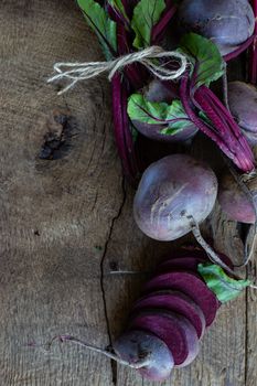 Bunch of fresh, spring, organic beetroot with slices of beetroot on old wooden background. Top view. Rustic, dramatic, organic kitchen. Ingredients, menu. Healthy life concept