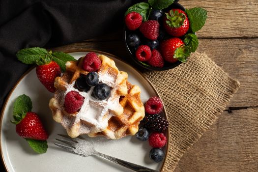 Belgian waffles with strawberries, summer berries on plate on dark old wooden dramatic background. Top view. Menu, banner, poster, mock up. Rustic vintage style of kitchen.