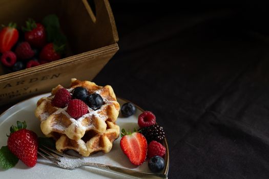 Belgian waffles with strawberries, summer berries on plate on dark old wooden dramatic background. Horizontal view. Menu, banner, poster, mock up. Rustic vintage style of kitchen.