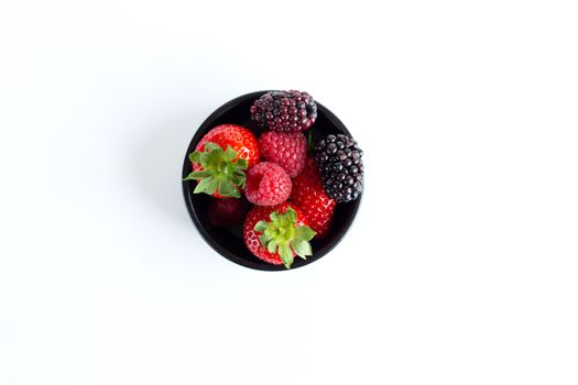 Fresh summer berries in black round bowls on white background. Close up, flat lay, copy space.