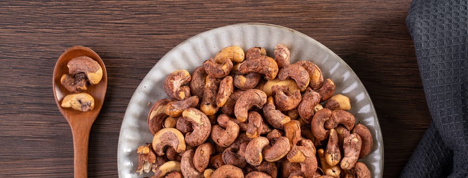 Cashew nuts with peel in a plate on wooden tray and table background, healthy raw food plate.