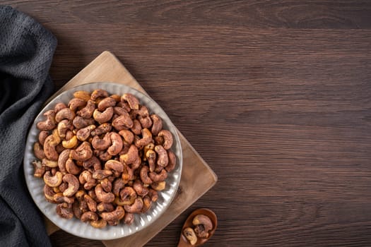 Cashew nuts with peel in a plate on wooden tray and table background, healthy raw food plate.