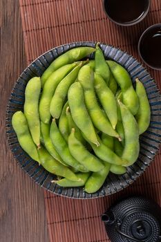 Fresh cooked boiled edamame in a plate on wooden tray and table background, healthy protein food concept.