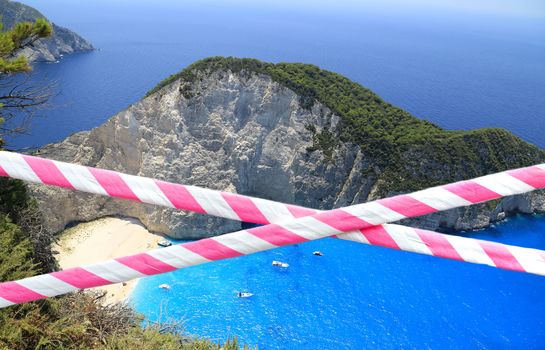 Red and white barrier tape ribbon across exotic beautiful beach background. Holiday concept, delayed travel, no more summer plans and home isolation due COVID-19 corona virus pandemic outbreak.