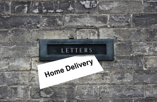 Daily magazine, letter with sign Home Delivery waiting to be picked up from the old door hole, letter box. Old brick house background. Horozontal, close up. Safety home delivery concept