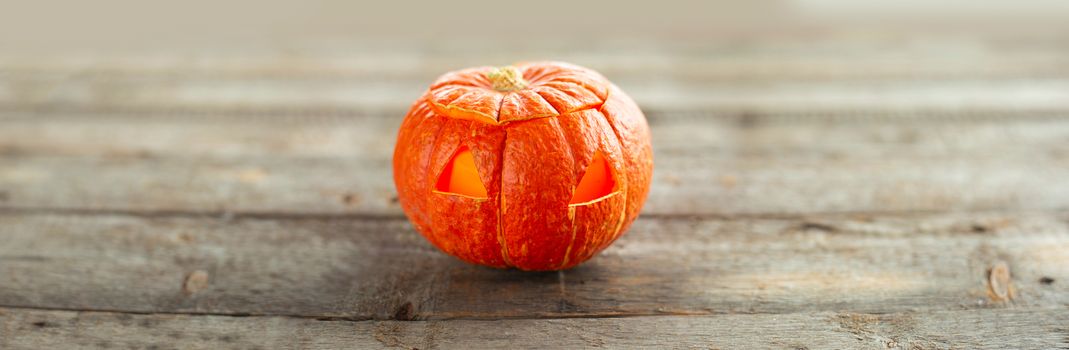 Minimalistic carved glowing Halloween pumpkin head jack lantern on wooden background with copy space gor text horizontal composition