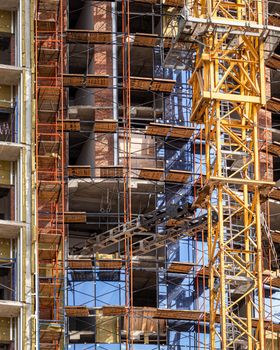 Fragment of an unfinished concrete and red brick building under construction with scaffolding and a crane.