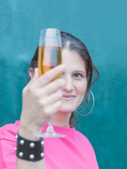 Girl with gathered hair and big hoop earring shows a glass of wine in front of her face, close up portrait of model on dark green background