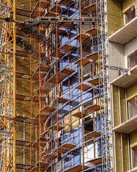 Fragment of an unfinished concrete and red brick building under construction with scaffolding and a crane.