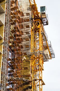 Fragment of an unfinished concrete and red brick building under construction with scaffolding and a crane.