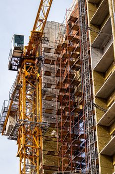 Fragment of an unfinished concrete and red brick building under construction with scaffolding and a crane.