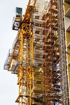 Fragment of an unfinished concrete and red brick building under construction with scaffolding and a crane.