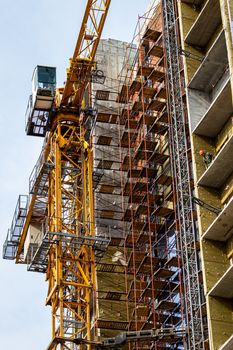 Fragment of an unfinished concrete and red brick building under construction with scaffolding and a crane.