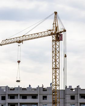 A team of construction workers in and a crane constructing a building on the background of the evening cloudy sky.