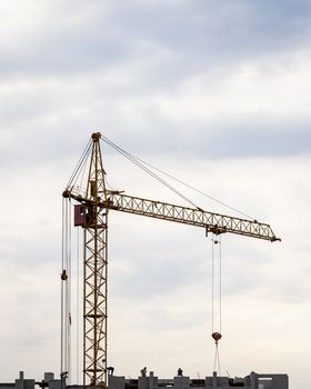 A team of construction workers in and a crane constructing a building on the background of the evening cloudy sky.