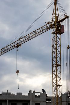 A team of construction workers in and a crane constructing a building on the background of the evening cloudy sky.