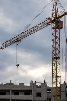 A team of construction workers in and a crane constructing a building on the background of the evening cloudy sky.