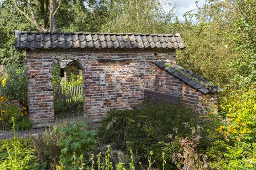ruin of an old stone shed with an arch as entrance surrounded by plants and flowers in a large green garden