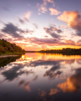 A sunset or sunrise scene over a lake or river with dramatic cloudy skies reflecting in the water on a summer evening or morning. Landscape.