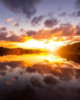 A sunset or sunrise scene over a lake or river with dramatic cloudy skies reflecting in the water on a summer evening or morning. Landscape.