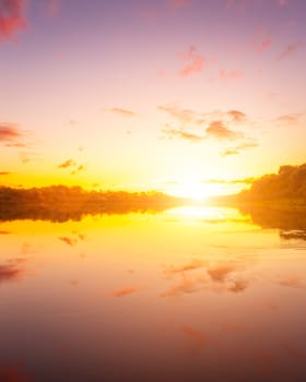 A sunset or sunrise scene over a lake or river with dramatic cloudy skies reflecting in the water on a summer evening or morning. Landscape.