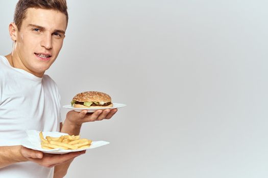 a man with fries and a hamburger on a light background in white t-shirt close-up cropped view Copy Space Model. High quality photo