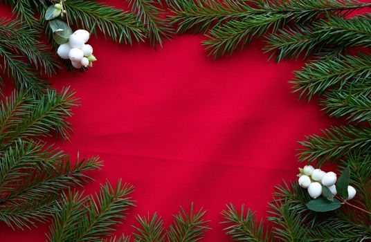 Frame of green fir branches and white dogwood berries on a red background. The concept of Christmas and the new year. Space for your text.