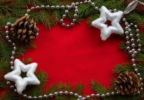 A frame of green fir branches ,two white stars and two cones with silver beads on a red background. The concept of Christmas and New year. Space for your text.