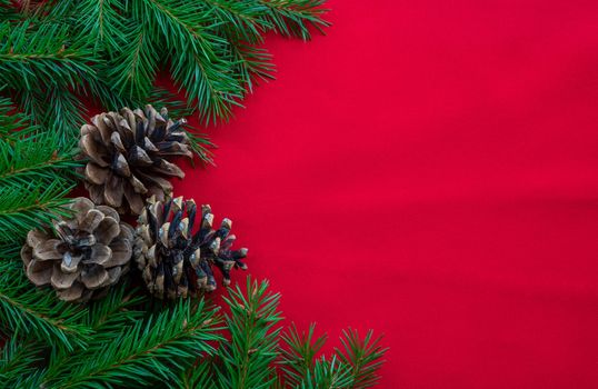 Christmas background with fir branches and three cones on a red canvas background. Christmas card. The theme of a winter holiday. Happy New Year. Space for text.