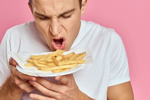 Man with French fries in a paper box on a pink background calories fast food portrait pink background. High quality photo