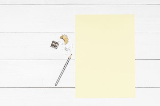 a pencil, a pencil sharpener and a yellow sheet of paper on a white wooden table