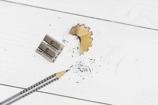 a pencil, a pencil sharpener and some shavings on a white wooden table